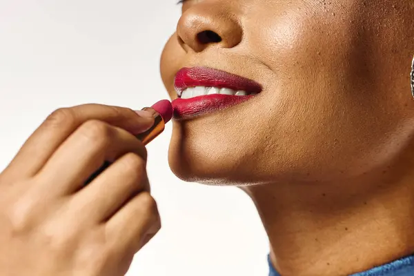 A beautiful african american woman smiles joyfully while applying bold lipstick. — Stock Photo