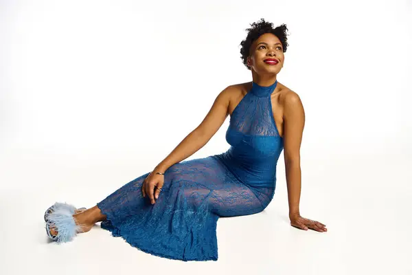 A stylish African American woman exudes confidence in her chic blue dress while seated. — Stock Photo