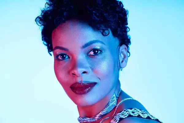 A chic African American woman exudes confidence with her trendy look amid vibrant blue lights. — Stock Photo