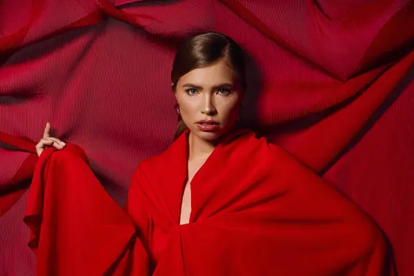 A stylish woman enchants with grace, draped in elegant red fabric for an artistic touch. — Stock Photo