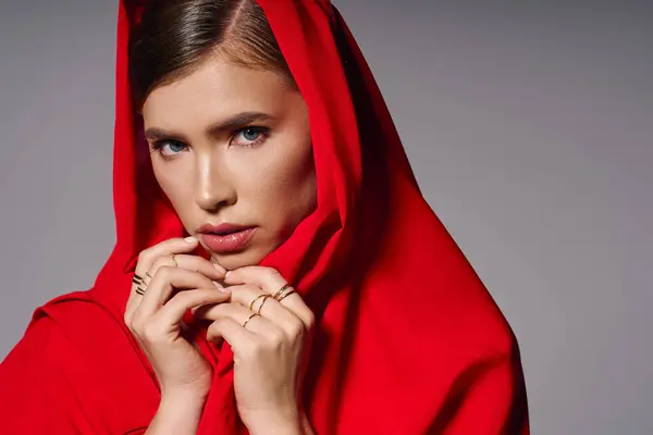Приголомшлива молода жінка в яскравому червоному капюшоні виділяє елегантність на фоні нейтрального фону. — стокове фото