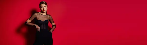 A young woman in a black outfit poses confidently against a bold red background. — Stock Photo