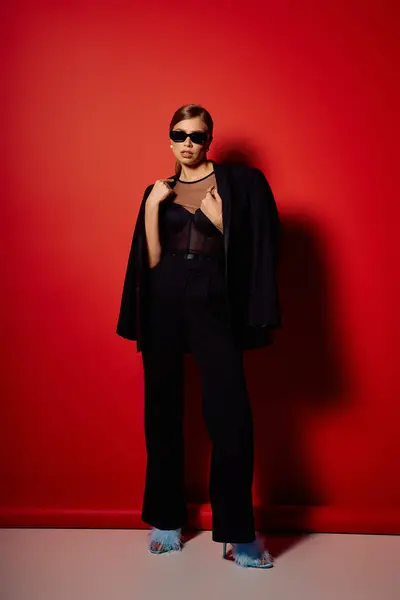 Chic young woman displays her style against a striking red backdrop, emphasizing elegance. — Stock Photo