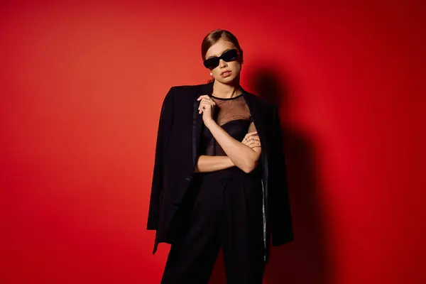 Young woman exudes confidence and style, showcasing elegance amid a vibrant red backdrop. — Stock Photo