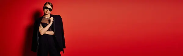 Una donna chic in bilico con un atteggiamento elegante, vestito elegantemente contro una parete rossa vibrante. — Foto stock