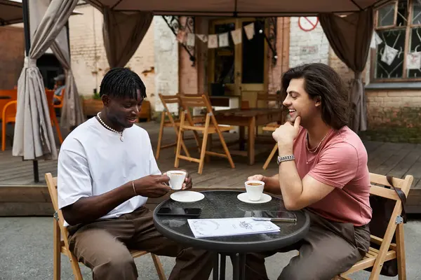 Dois homens encantadores sentam-se em um café acolhedor, compartilhando sorrisos e café em seu encontro. — Fotografia de Stock