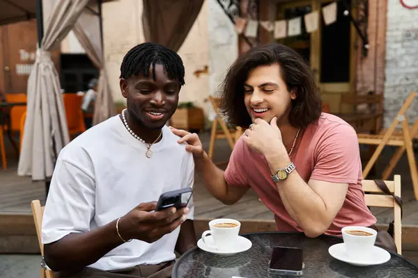 Two charming men share a delightful moment at a cafe, looking at a phone and smiling together. — Stock Photo