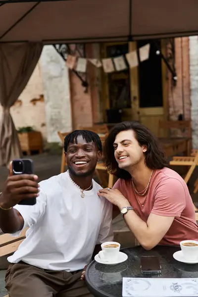 Two loving men smile brightly while taking a selfie during their delightful cafe date together. — Stock Photo