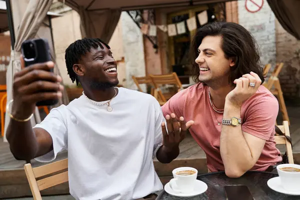 Two handsome men share laughter and love while enjoying coffee on a sunny date in a charming cafe. — Stock Photo