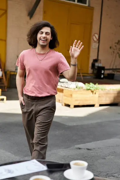 Young handsome man with long hair waving while in cafe. — Stock Photo