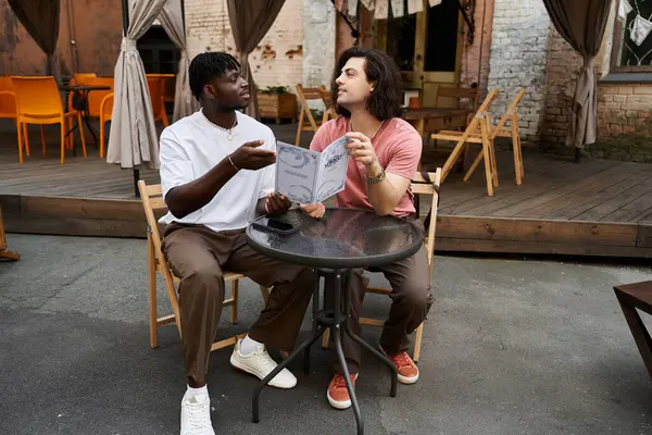 Two handsome men share a joyful moment over drinks while exploring the cafe menu together — Stock Photo