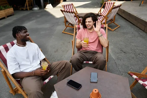 Two handsome men share laughter and joy during a delightful date at a serene outdoor cafe. — Stock Photo