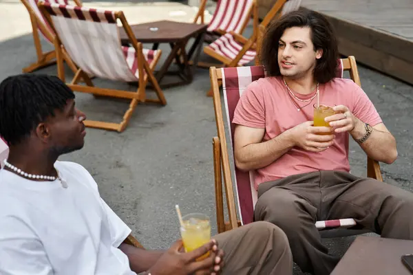 Two charming men enjoy each others company while sipping refreshing drinks on a warm day outdoors. — Stock Photo