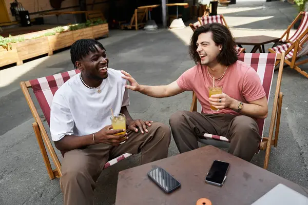 Two handsome men are engrossed in a joyful conversation over drinks at a cafe on a sunny day. — Stock Photo