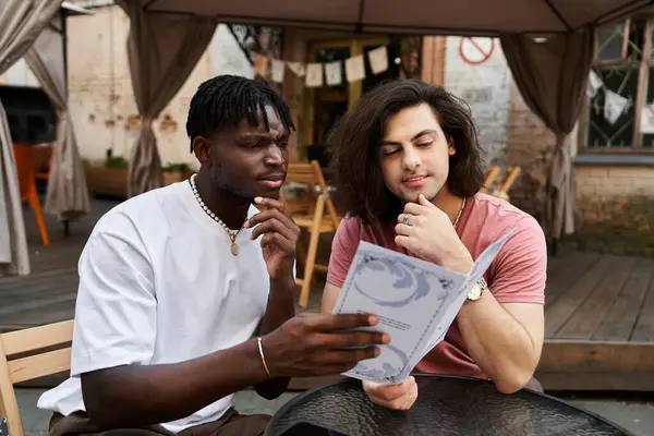 Two handsome men enjoy each others company as they browse the menu in a charming cafe garden. — Stock Photo