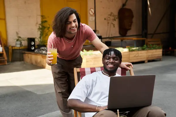 Two handsome men share laughs and drinks at a cafe while working on a laptop. — Stock Photo