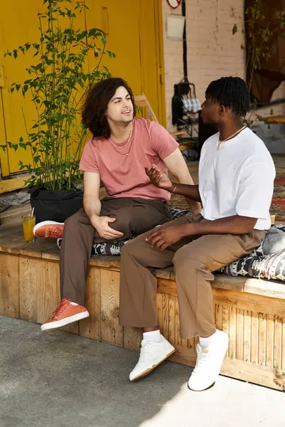 A joyful gay couple shares smiles and stories over drinks at a lively cafe. — Stock Photo