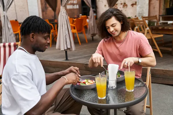 Due bei uomini condividono un momento gioioso durante il pranzo in un incantevole bar con decorazioni vivaci. — Foto stock