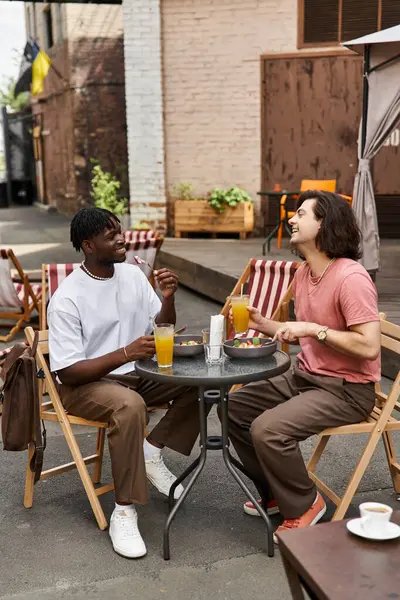 Due bei uomini condividono risate e deliziose bevande mentre pranzano insieme in un vivace caffè. — Foto stock