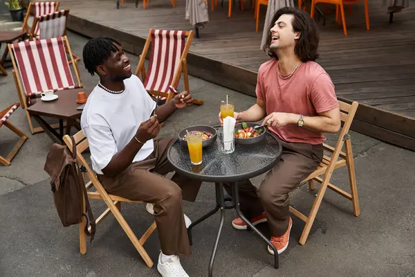 Two handsome men enjoy their romantic date, laughing while sharing tasty dishes and drinks. — Stock Photo