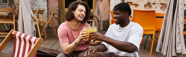 Two happy men toast with colorful drinks in a vibrant cafe, sharing smiles on their special date. — Stock Photo