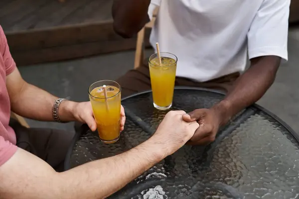 Dois homens bonitos compartilham um toque terno enquanto bebem bebidas refrescantes em uma atmosfera animada de café. — Fotografia de Stock