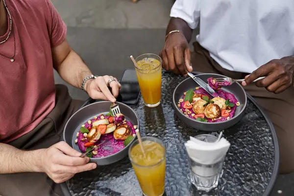 Two handsome men share a joyful moment at a cafe, savoring colorful meals and drinks together. — Stock Photo