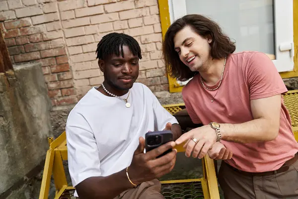 Two handsome men share smiles and stories while checking their phones together in a quaint cafe. — Stock Photo