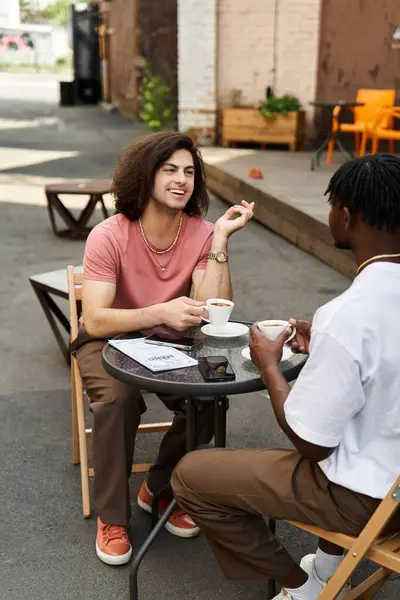 Two charming men share laughs at a cozy outdoor cafe table over drinks. — Stock Photo