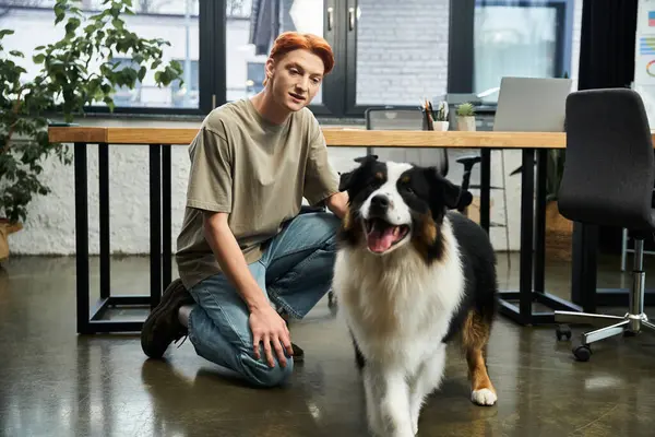 A dedicated young man with red hair interacts with a vibrant dog in a stylish work environment. — Stock Photo