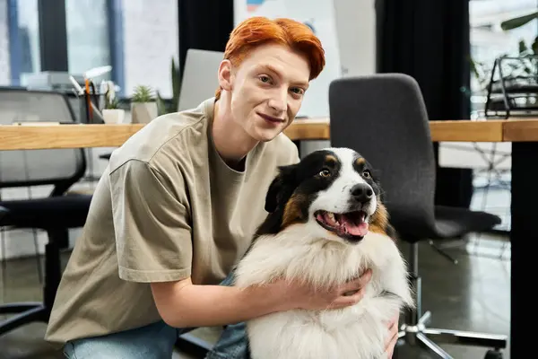 A young man with striking red hair interacts joyfully with a friendly dog in a stylish office. — Stock Photo