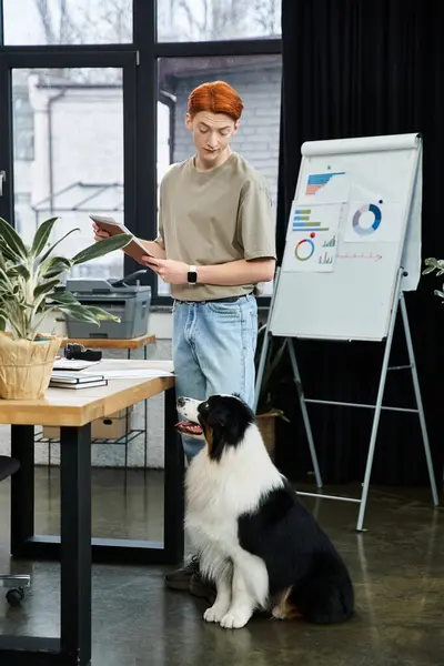 A dedicated young man with red hair works in a stylish office with his dog by his side. — Stock Photo