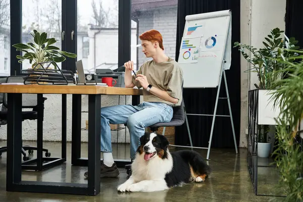 A young red haired man works diligently on his laptop in a modern office with plants. — Stock Photo
