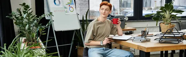 Young man with ginger hair enjoys coffee while working in a creative office. — Stock Photo