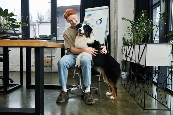 A red haired young man shares a warm moment with his furry friend in a modern office. — Stock Photo