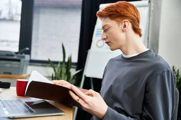 In a modern office, a young red haired man thoughtfully studies papers at his desk. — Stock Photo