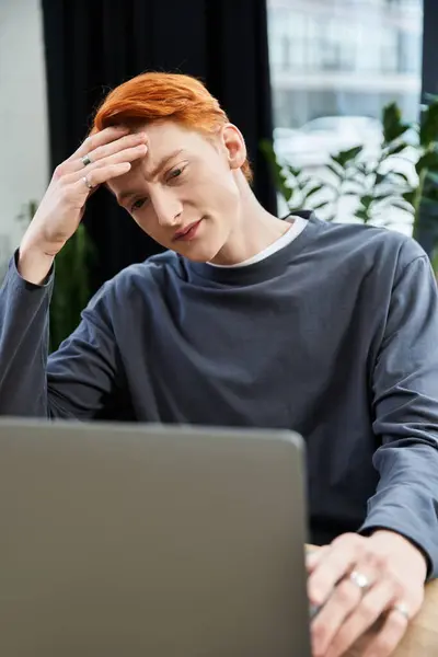 A young man with striking red hair is deeply engaged in his work, showing dedication at the office. — Stock Photo