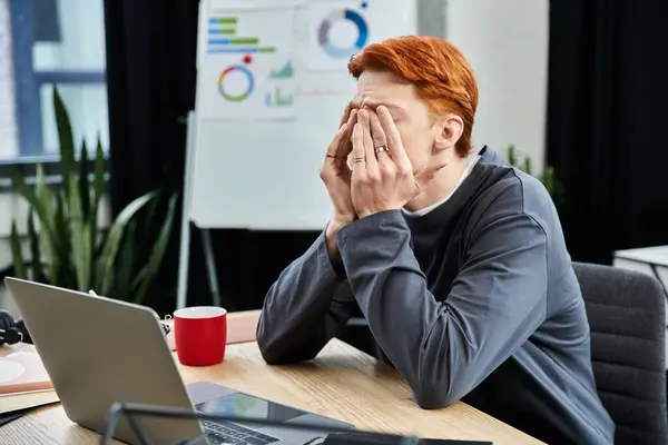 A young man with red hair covers his face at his desk, overwhelmed by work stress. — Stock Photo