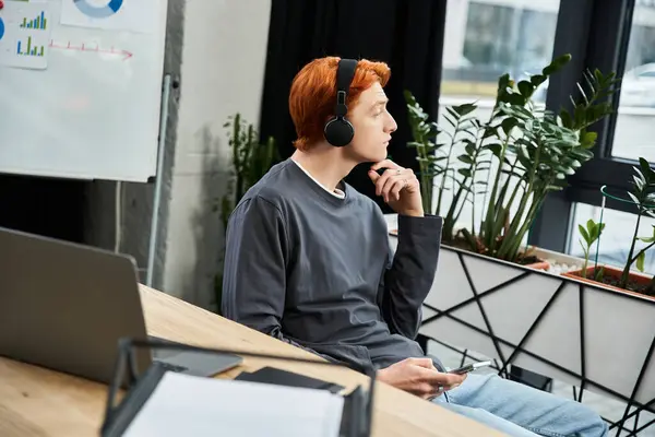 A young man with red hair reflects deeply while working in a contemporary office setting. — Stock Photo