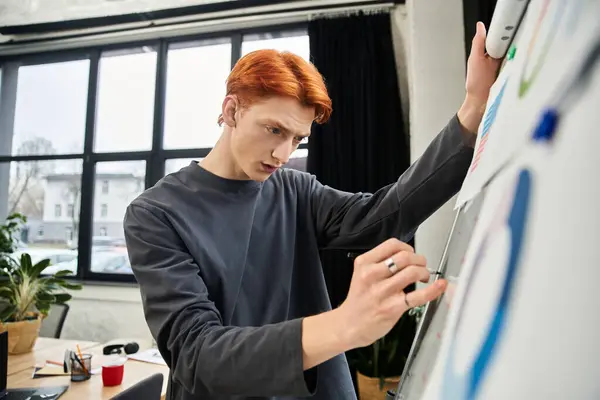 Jovem focado com cabelo vermelho trabalha diligentemente em um projeto em um ambiente de escritório contemporâneo. — Fotografia de Stock