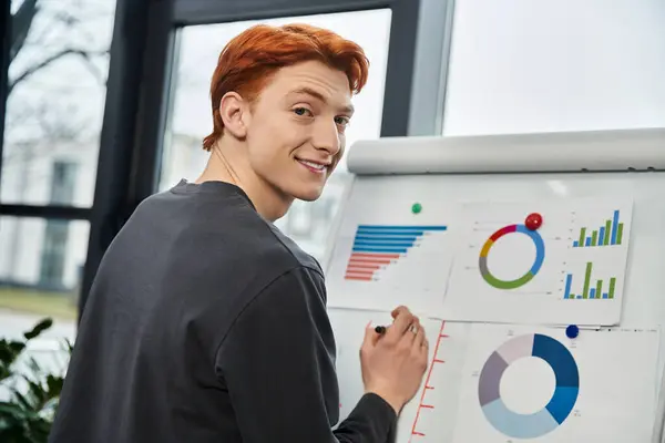 Red haired man actively presents data visuals on a whiteboard in a bright office space. — Stock Photo