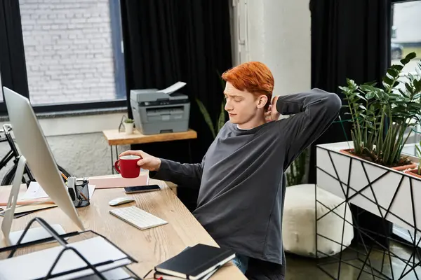Un joven profesional dedicado con el pelo rojo toma un breve descanso en su escritorio. - foto de stock