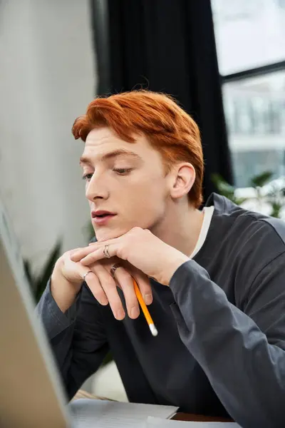 Young man with striking red hair concentrates deeply while sitting at a desk in the office — Stock Photo