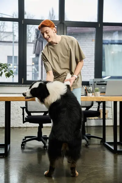 A dedicated young red haired man shares a joyful moment with a dog at his workspace. — Stock Photo