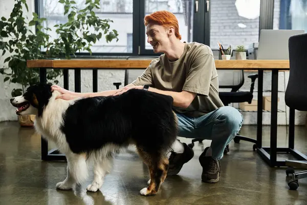 A young man with red hair shares a moment of joy with a dog amidst a bustling office setting. — Stock Photo