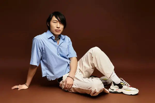 A fashionable asian man relaxes in a contemporary studio, showcasing his unique style. — Stock Photo