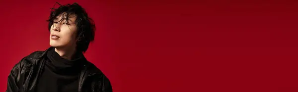 Stylish Asian man in black leather jacket poses on red, banner — Stock Photo