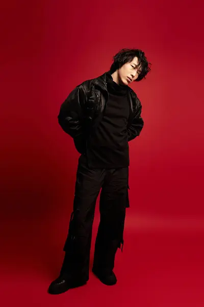Jovem asiático homem golpeia uma pose de moda contra um pano de fundo vermelho em elegante vestuário preto. — Fotografia de Stock