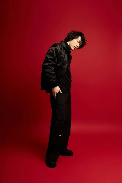 Young Asian man in black strikes a stylish pose in a vibrant red studio. — Stock Photo