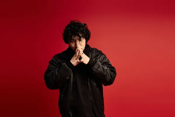 Stylish Asian man in black poses with hands together on red. — Stock Photo